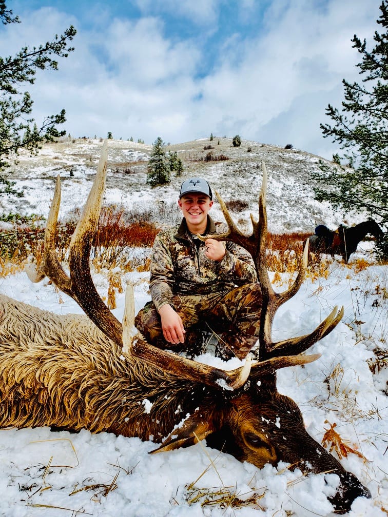 A hunter kneels in the snow next to a harvested elk.