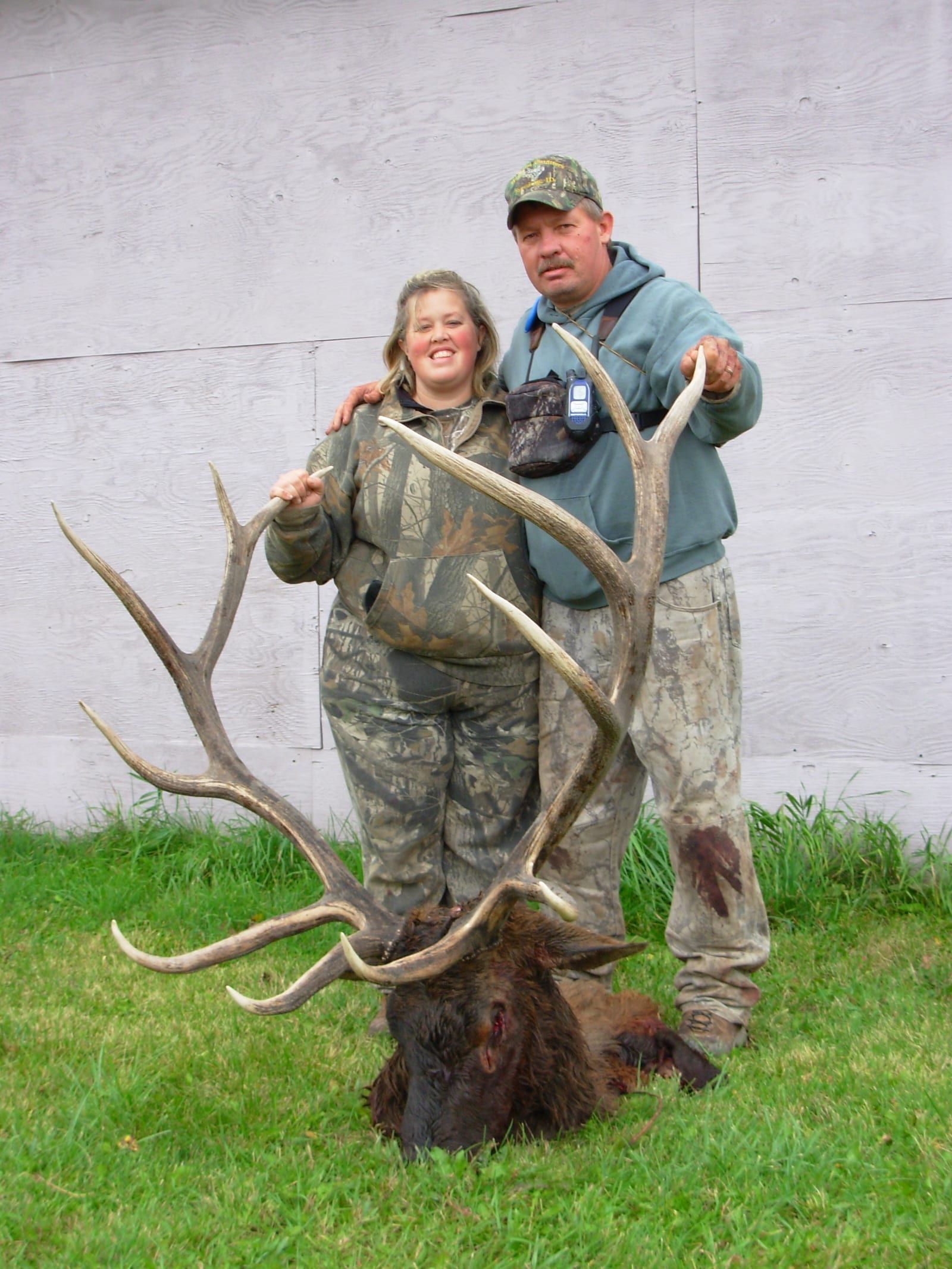 A man and a woman in camouflage clothing pose with a harvested elk.