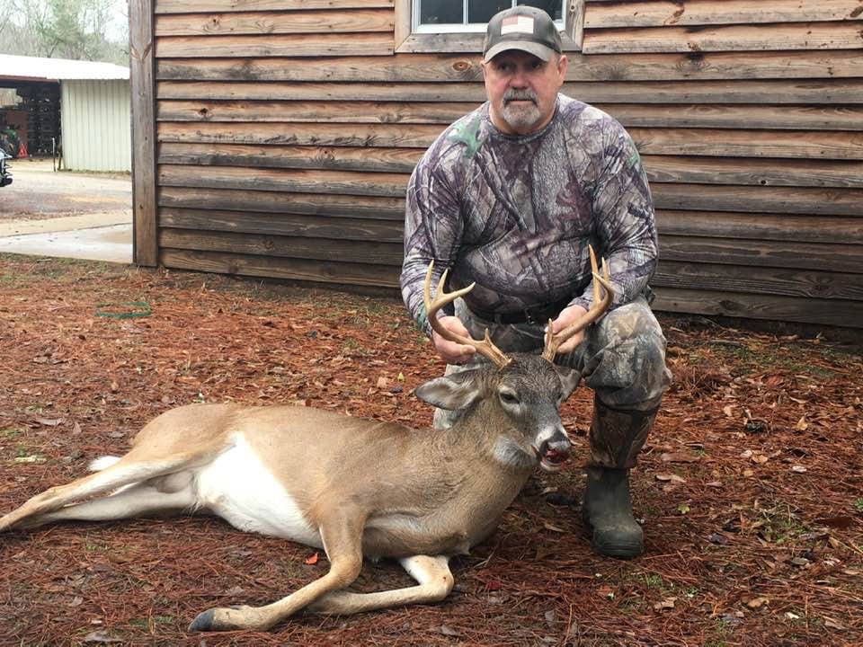 A hunter kneels next to a harvested whitetail deer on a bed of pine needles.