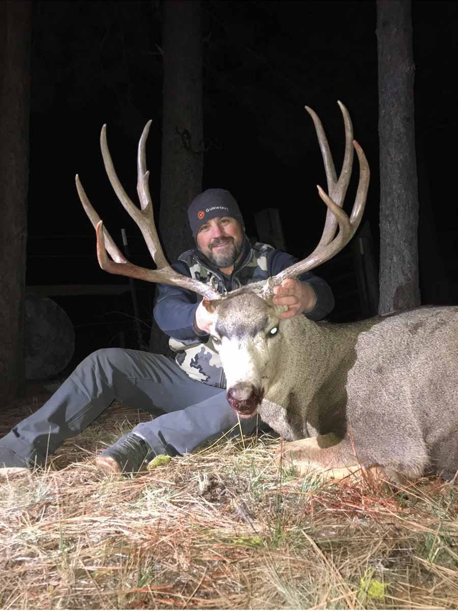 A hunter poses with a harvested mule deer at night.