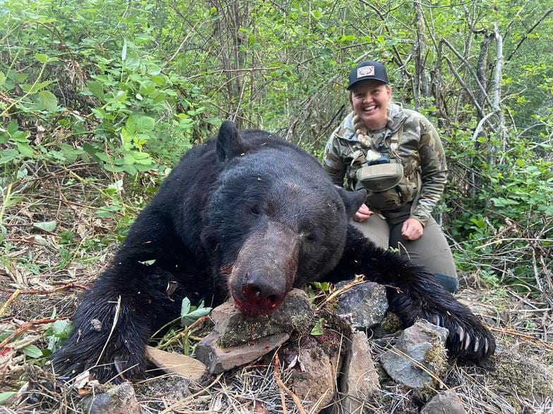 A hunter poses with a harvested black bear in a forest.
