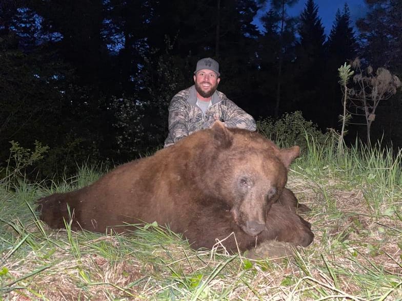 A hunter poses with a harvested black bear at night.