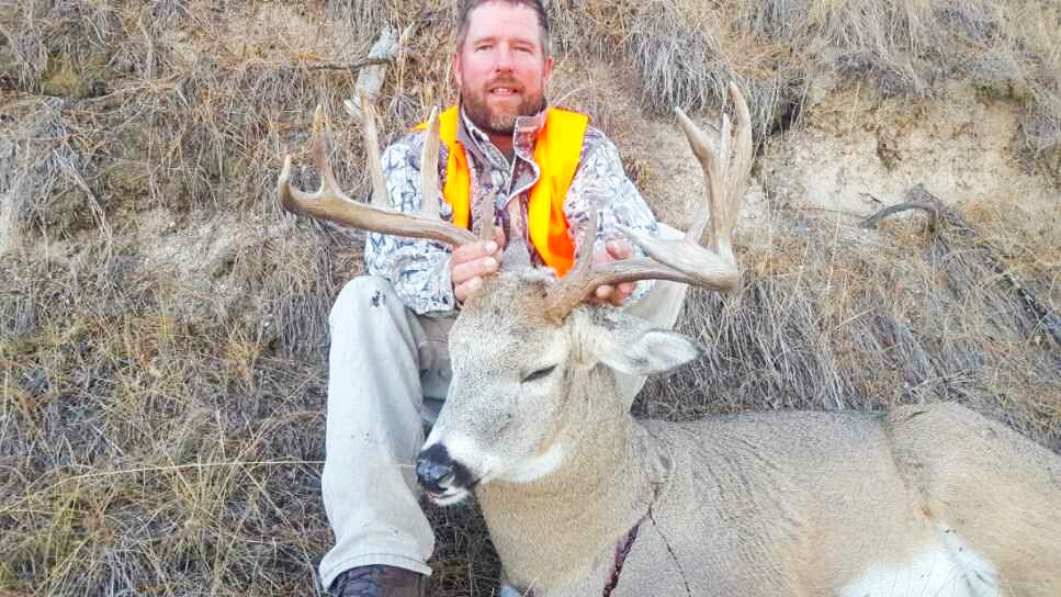A hunter kneels next to a harvested mule deer.