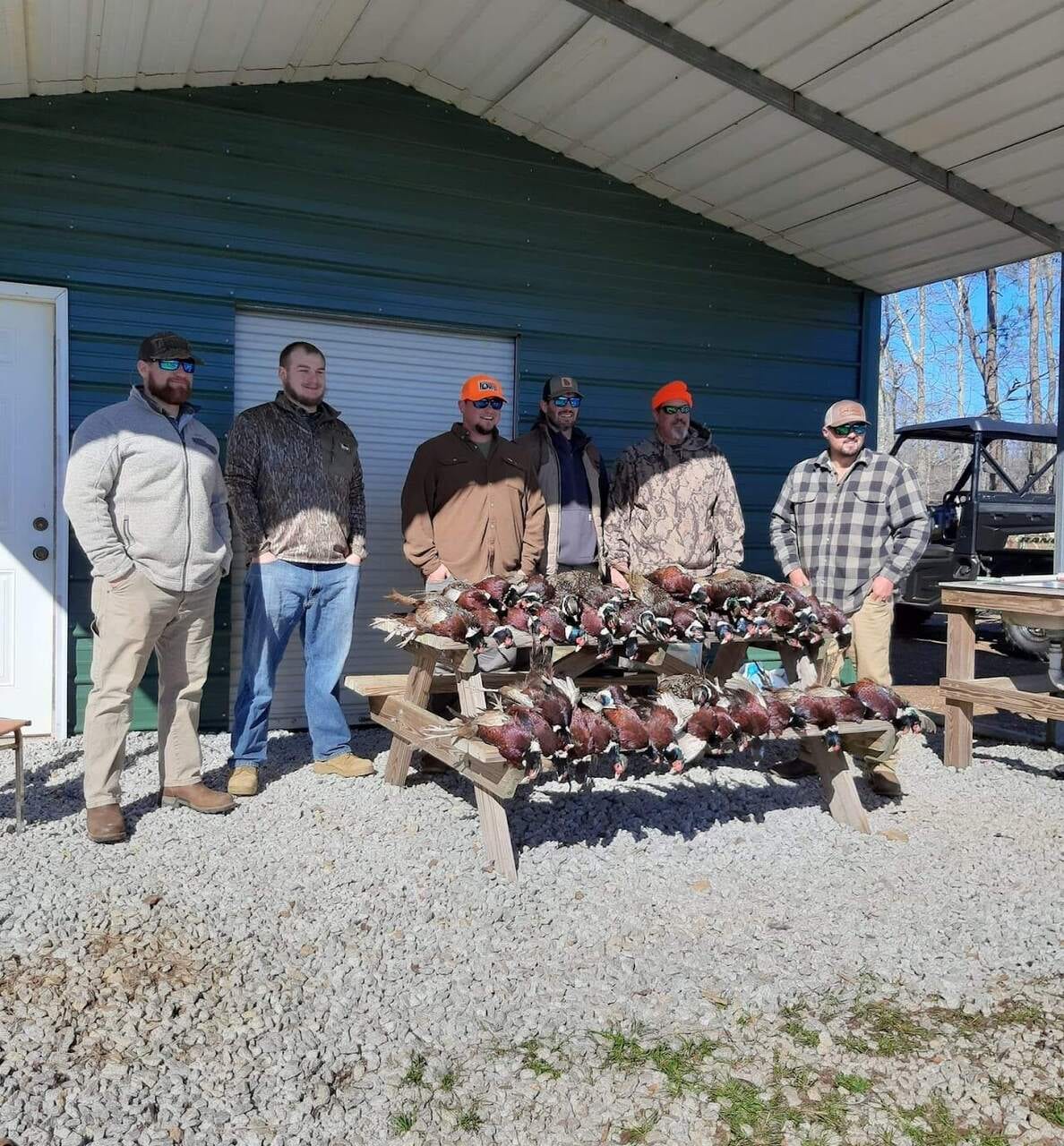 Six hunters behind a picnic table loaded with harvested pheasants and quail