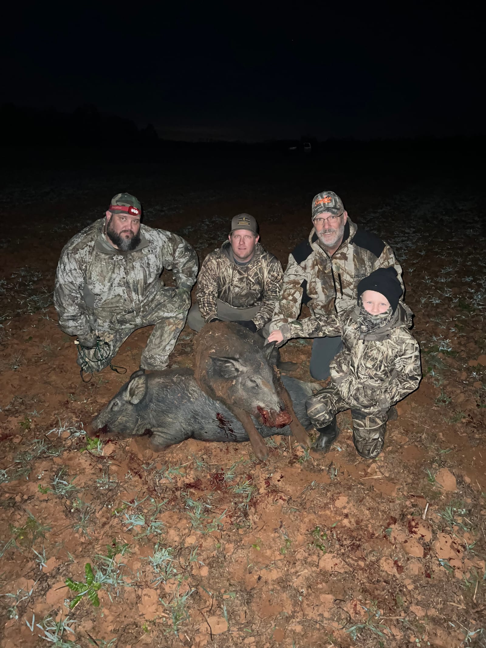 Four hunters pose with two harvested wild boars at night.