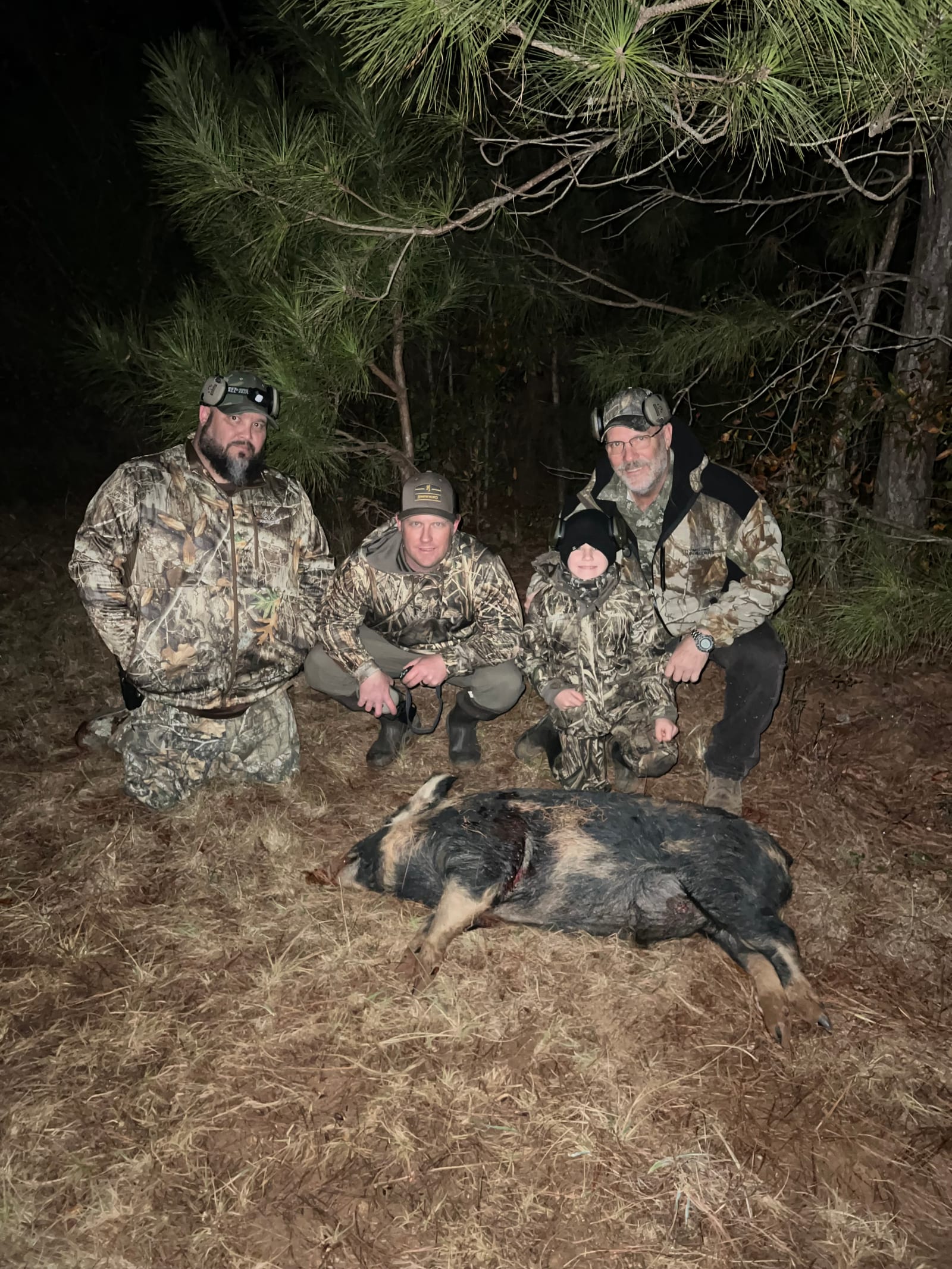 Four hunters, including a child, pose with a harvested wild boar at night.