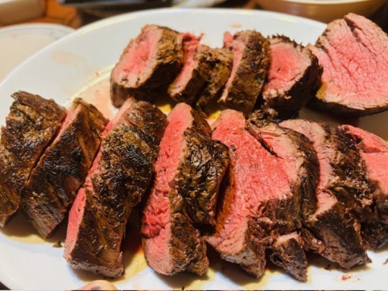 Slices of cooked meat are arranged on a white plate.