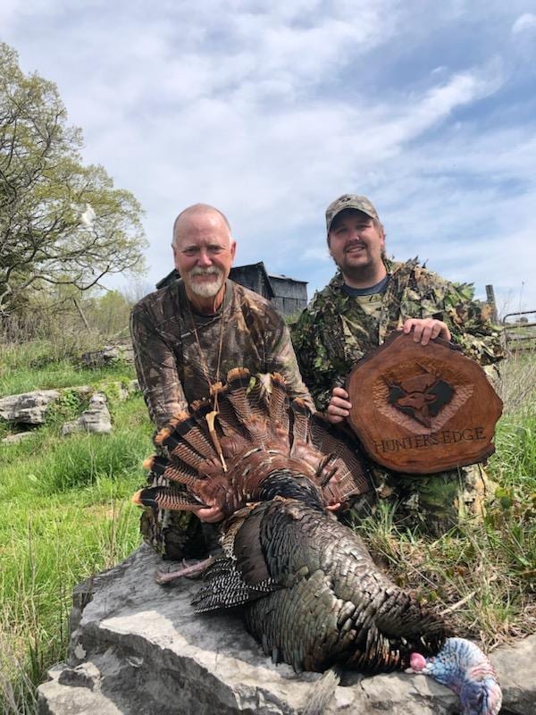 Two hunters pose with a harvested wild turkey.