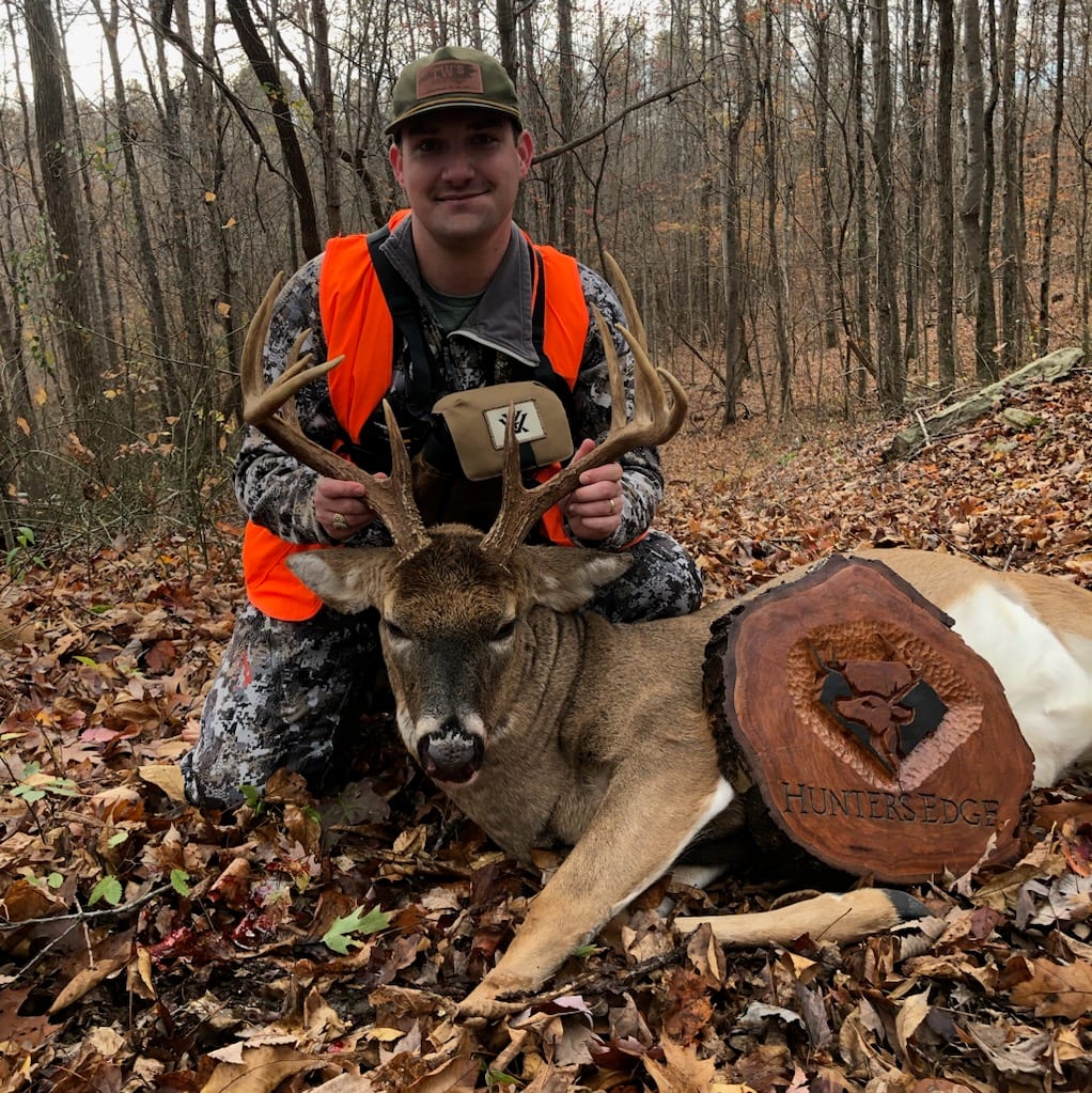 A hunter kneels next to a harvested whitetail deer in a forest setting.