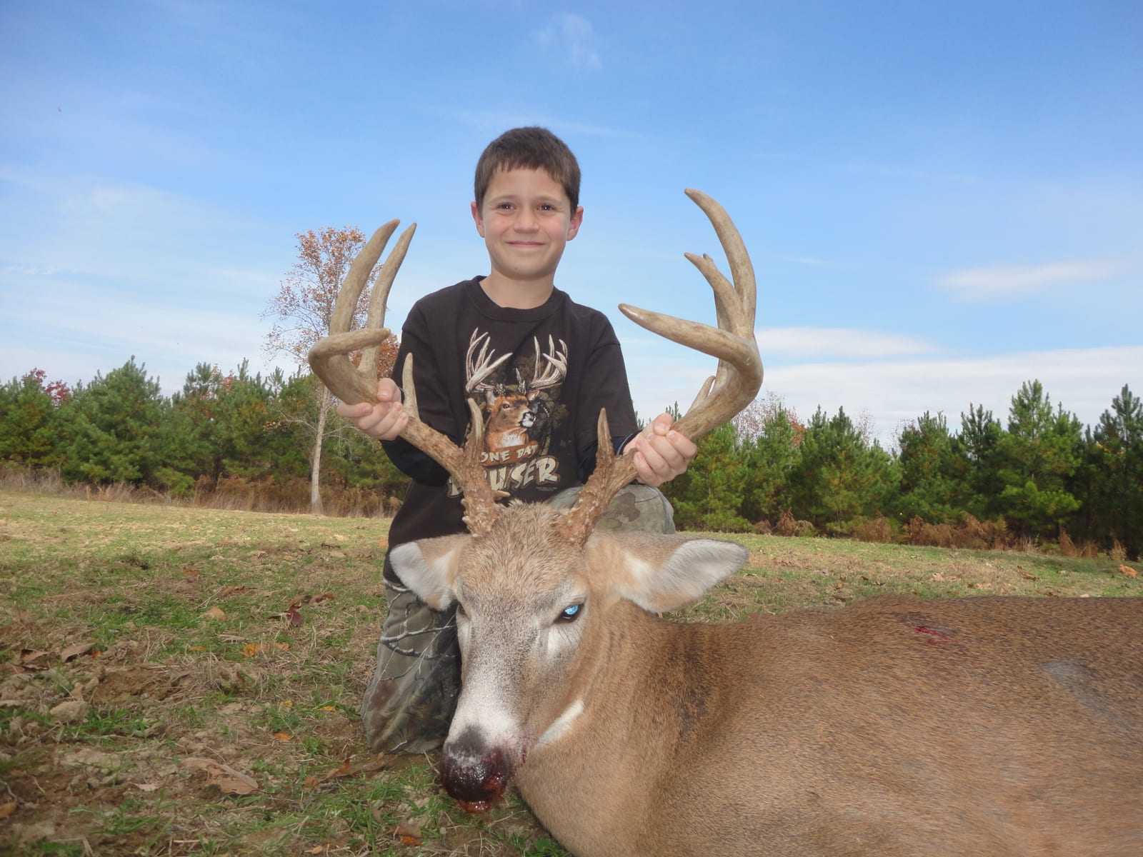 A young boy poses with a harvested whitetail deer in a field.