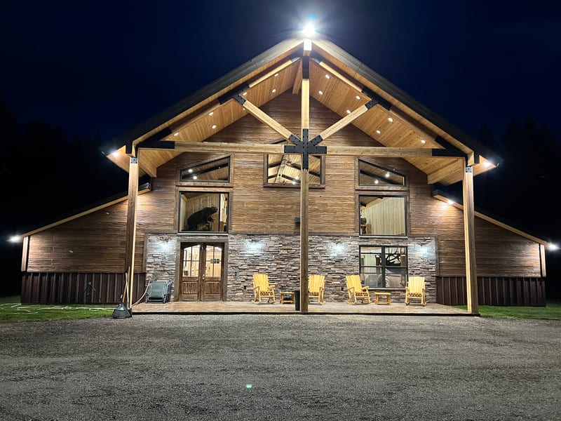 A large, illuminated wooden lodge with stone accents and outdoor seating at night.