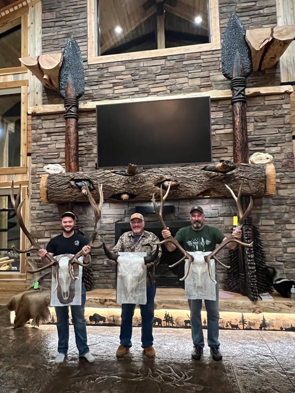 Three men pose with elk antlers and skulls in a lodge.