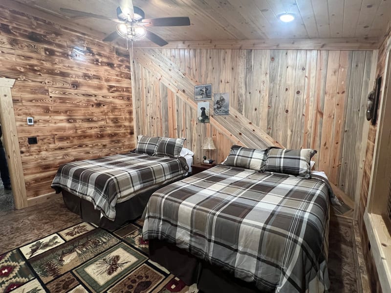 A bedroom with two beds, plaid bedding, and wood-paneled walls.