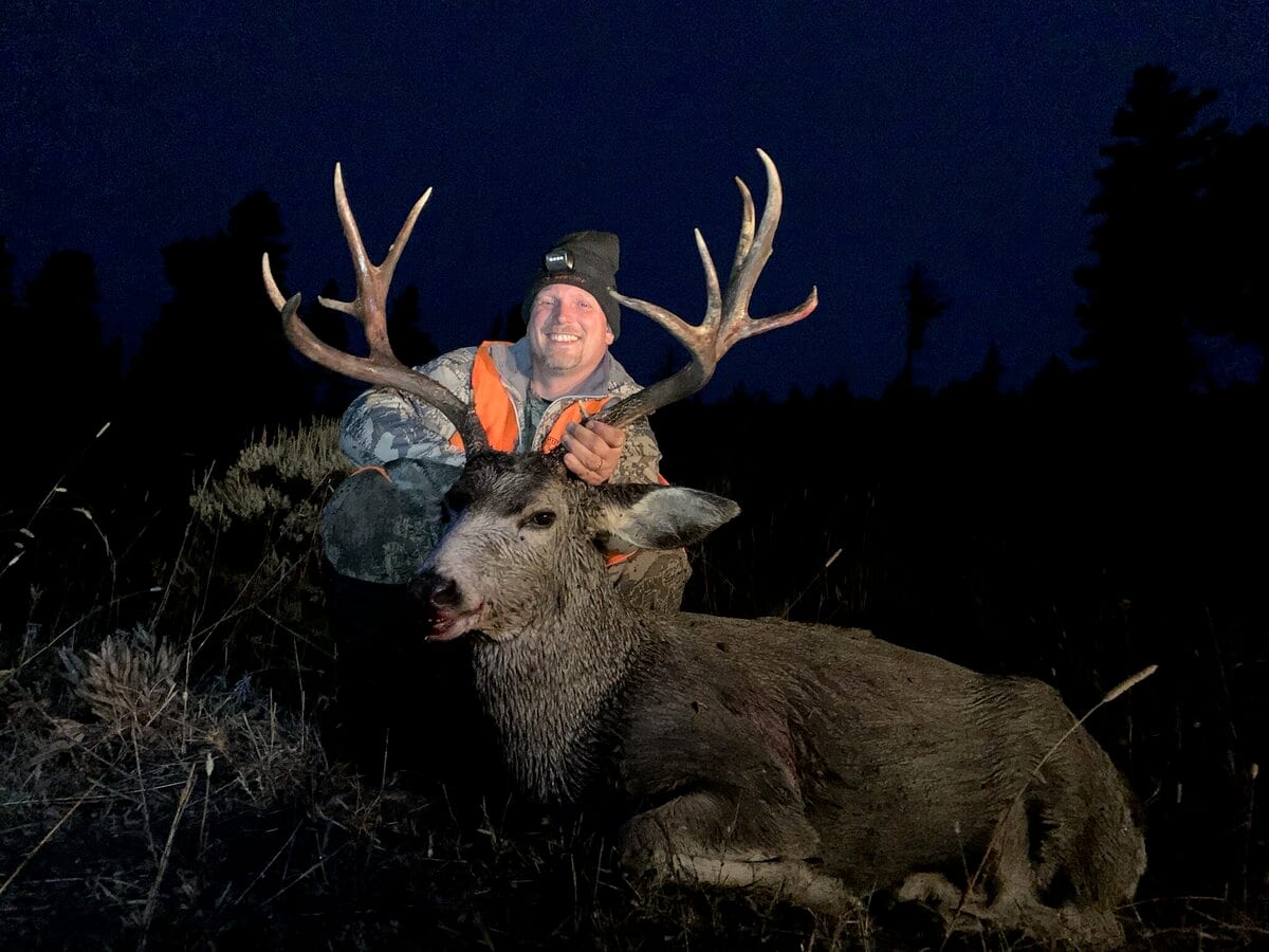 A hunter poses with a harvested mule deer at night.