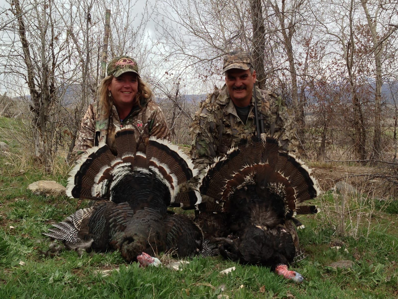 Two hunters pose with two harvested wild turkeys.