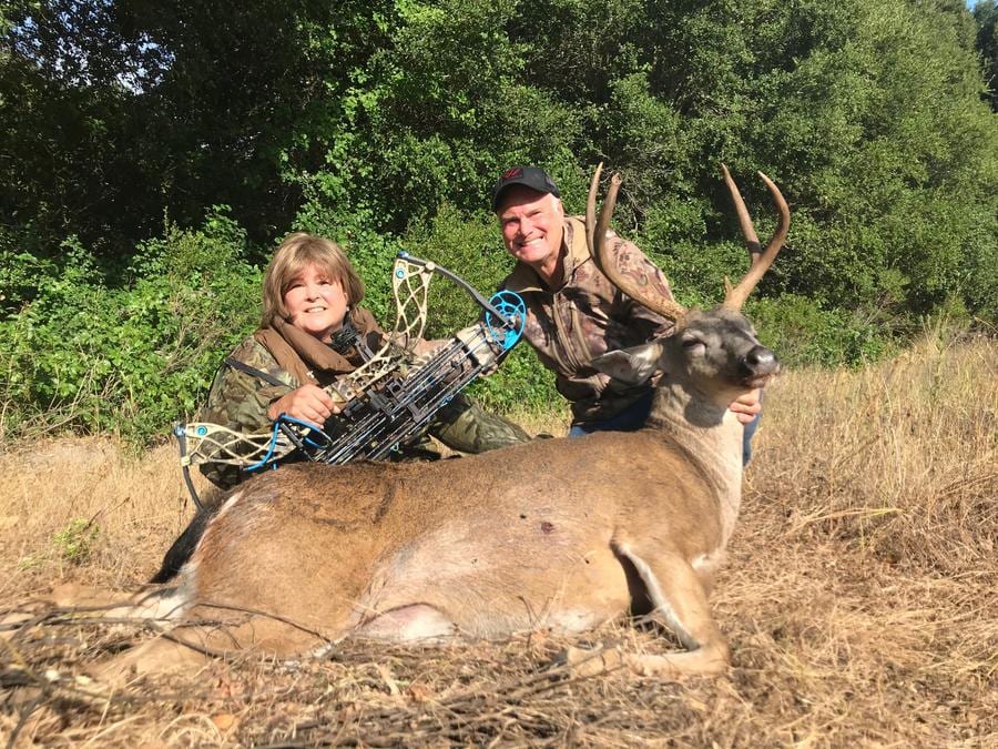 A man and a woman pose with a harvested deer and a bow.