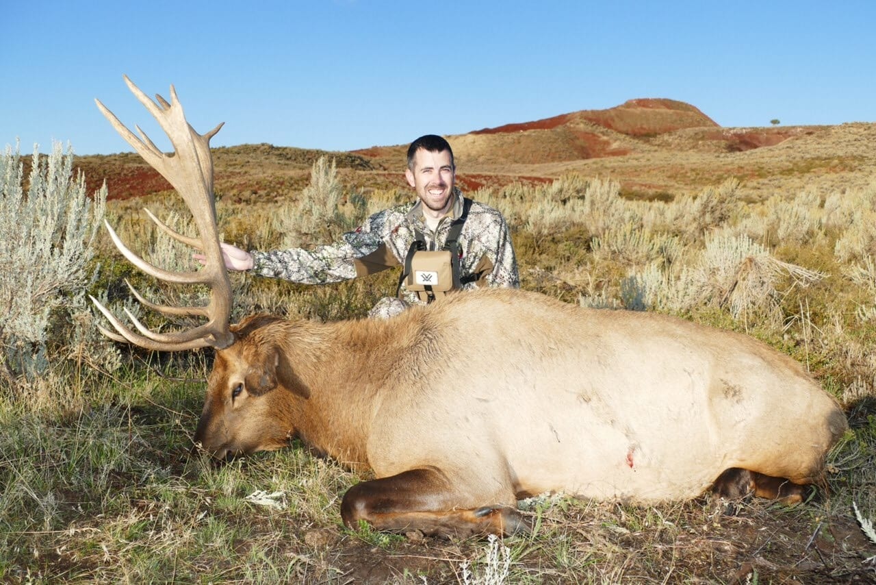 A hunter poses with a harvested elk in a field.