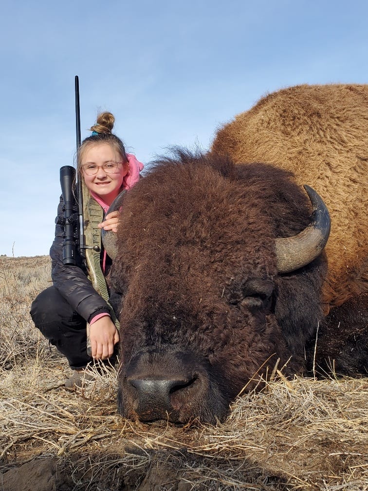 A young girl poses with a harvested bison.
