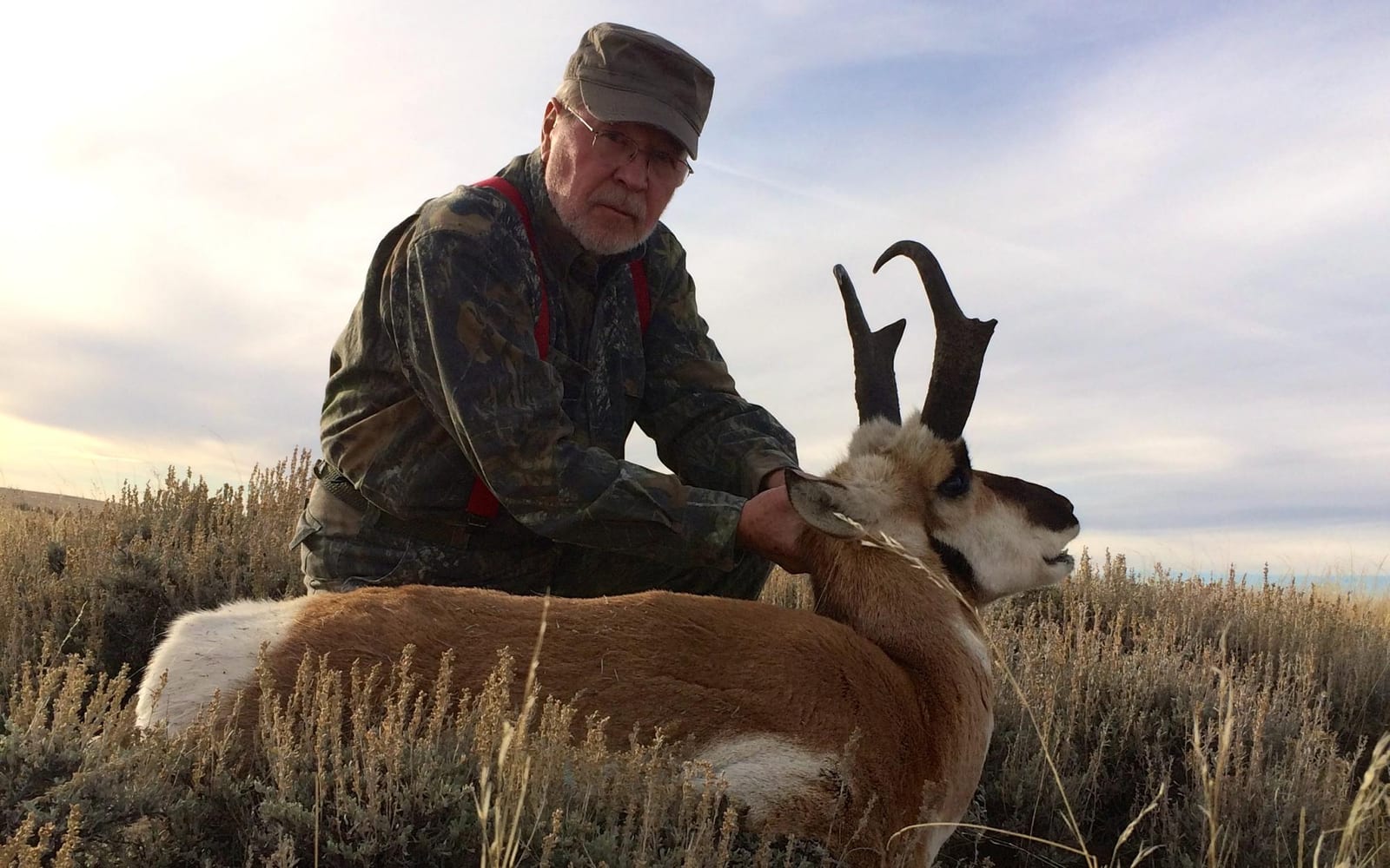 A hunter kneels next to a harvested pronghorn in a field.