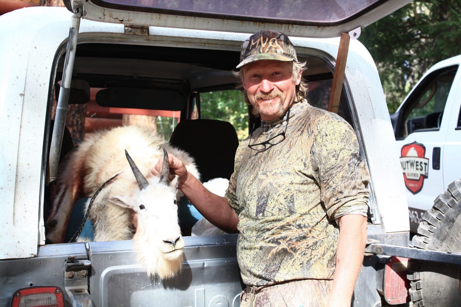 A hunter poses with a harvested mountain goat in the back of a vehicle.