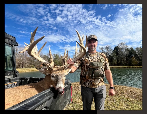 A man standing with his trophy whitetail deer in the back of a 4 wheeler