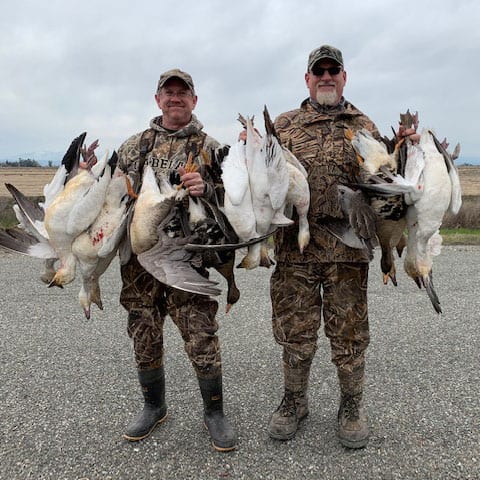 Two hunters pose with their harvest of snow geese and white-fronted geese.
