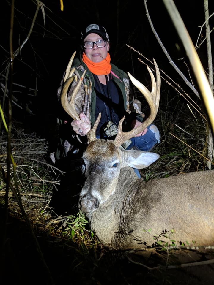 A woman poses with a harvested whitetail deer at night.