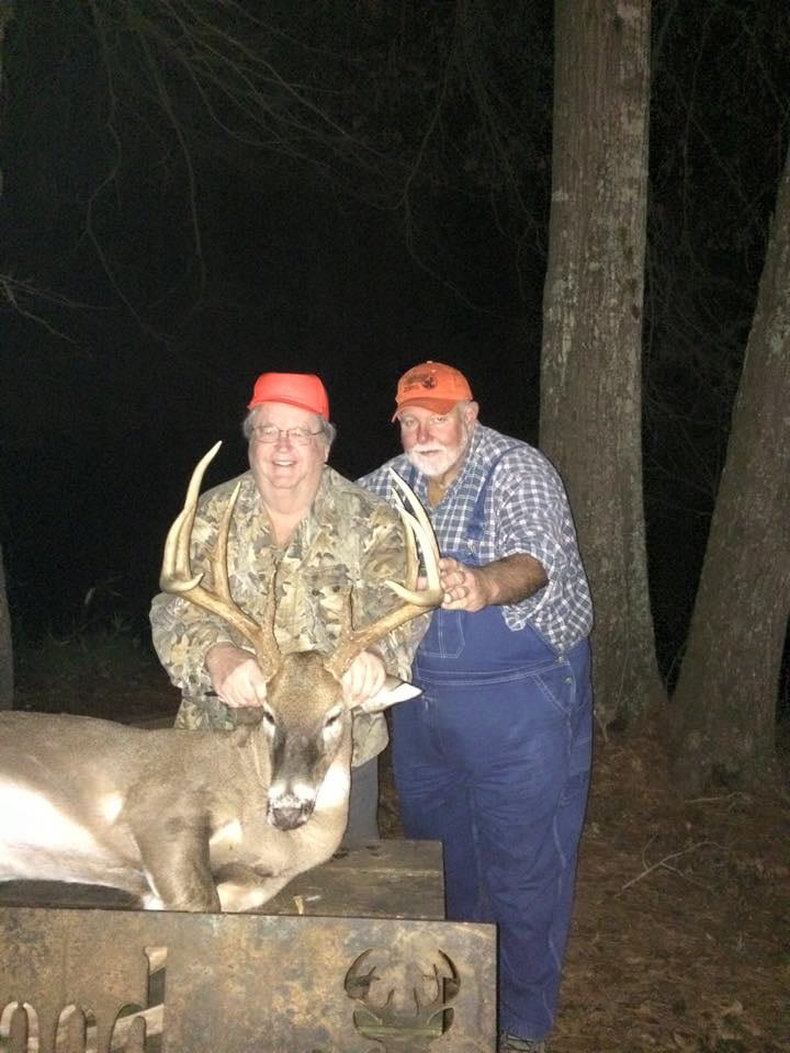Two men in hunting attire pose with a harvested whitetail deer at night.