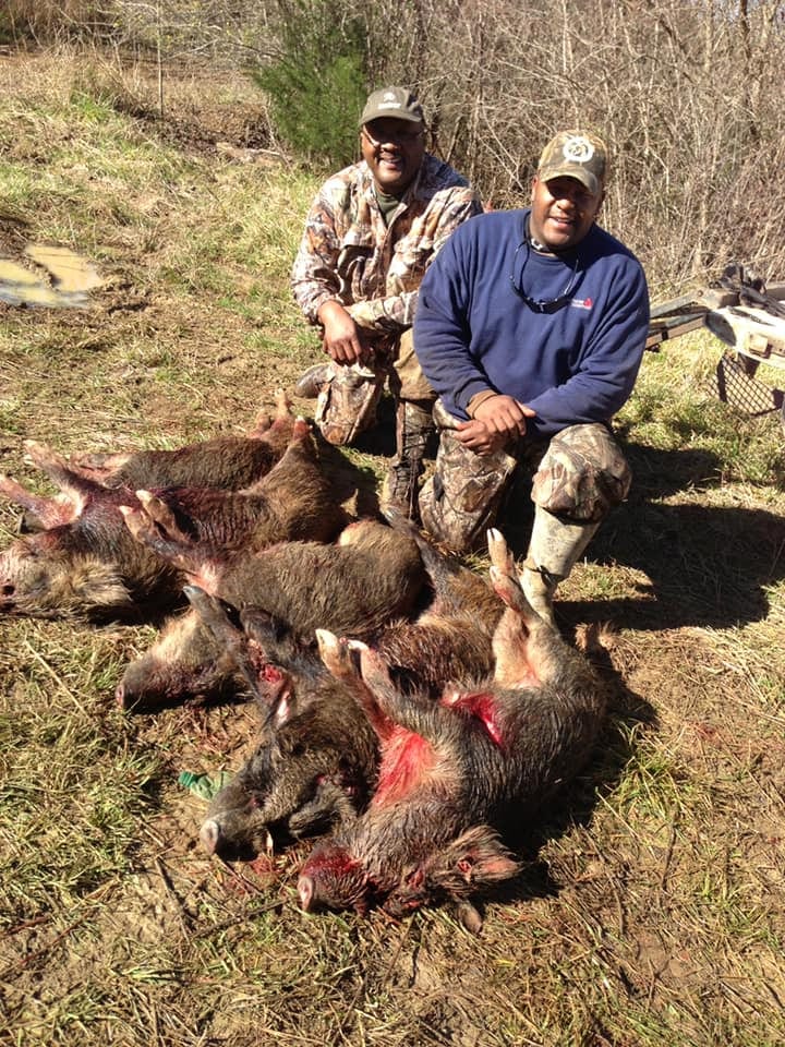 Two hunters pose with several harvested wild boars on the ground.