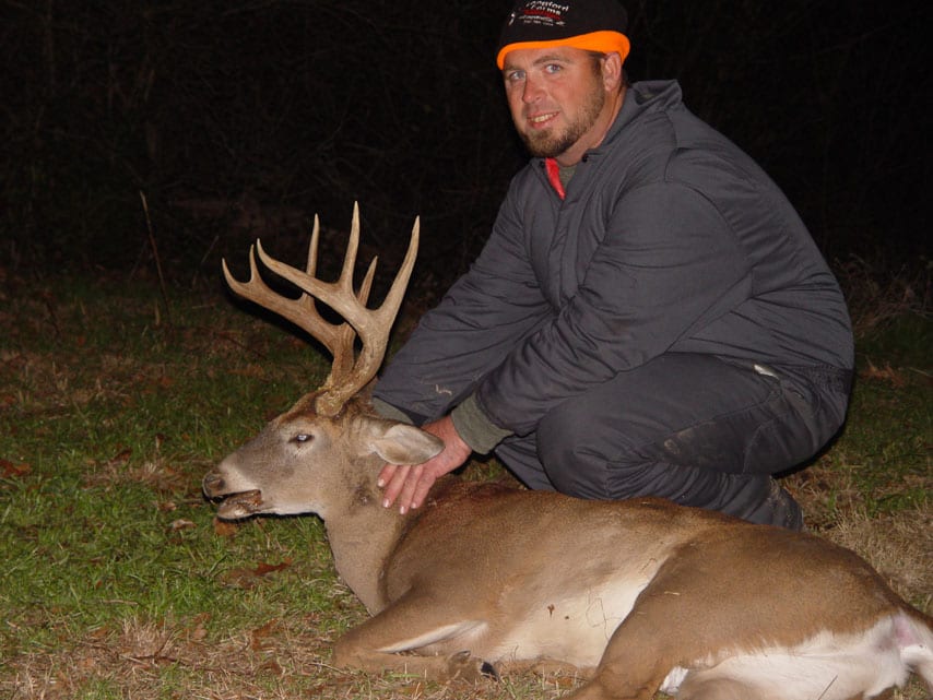 A hunter kneels next to a harvested whitetail deer at night.