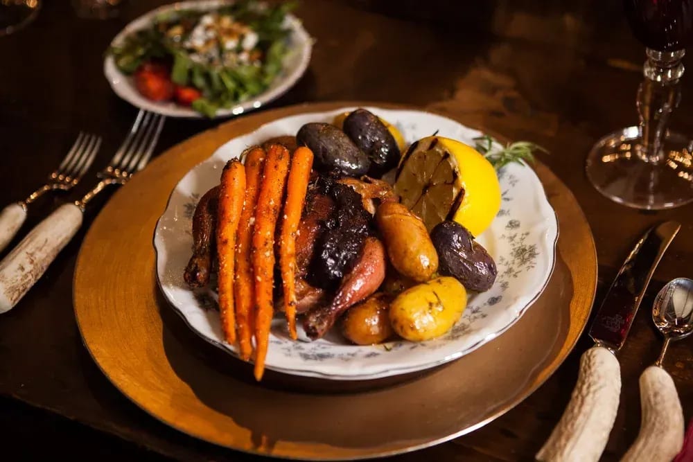 Plated roasted vegetables and meat on a dining table with utensils and a glass nearby