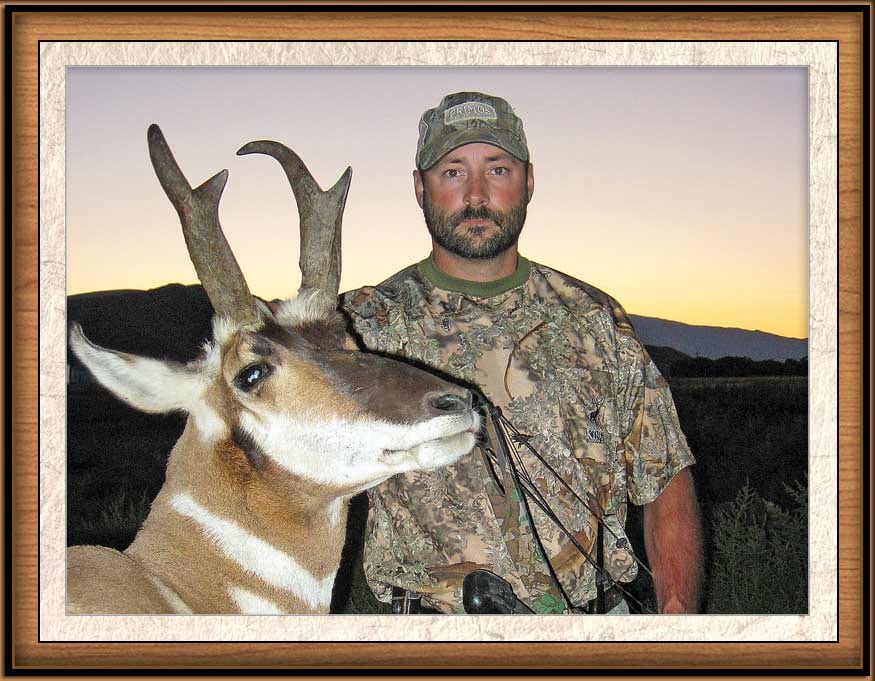 A hunter poses with a harvested pronghorn at sunset.