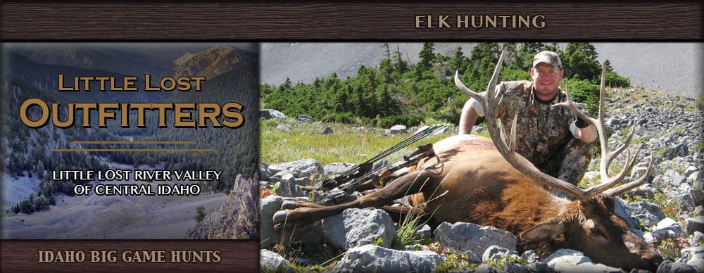 A hunter poses with a harvested elk in a rocky, mountainous landscape.