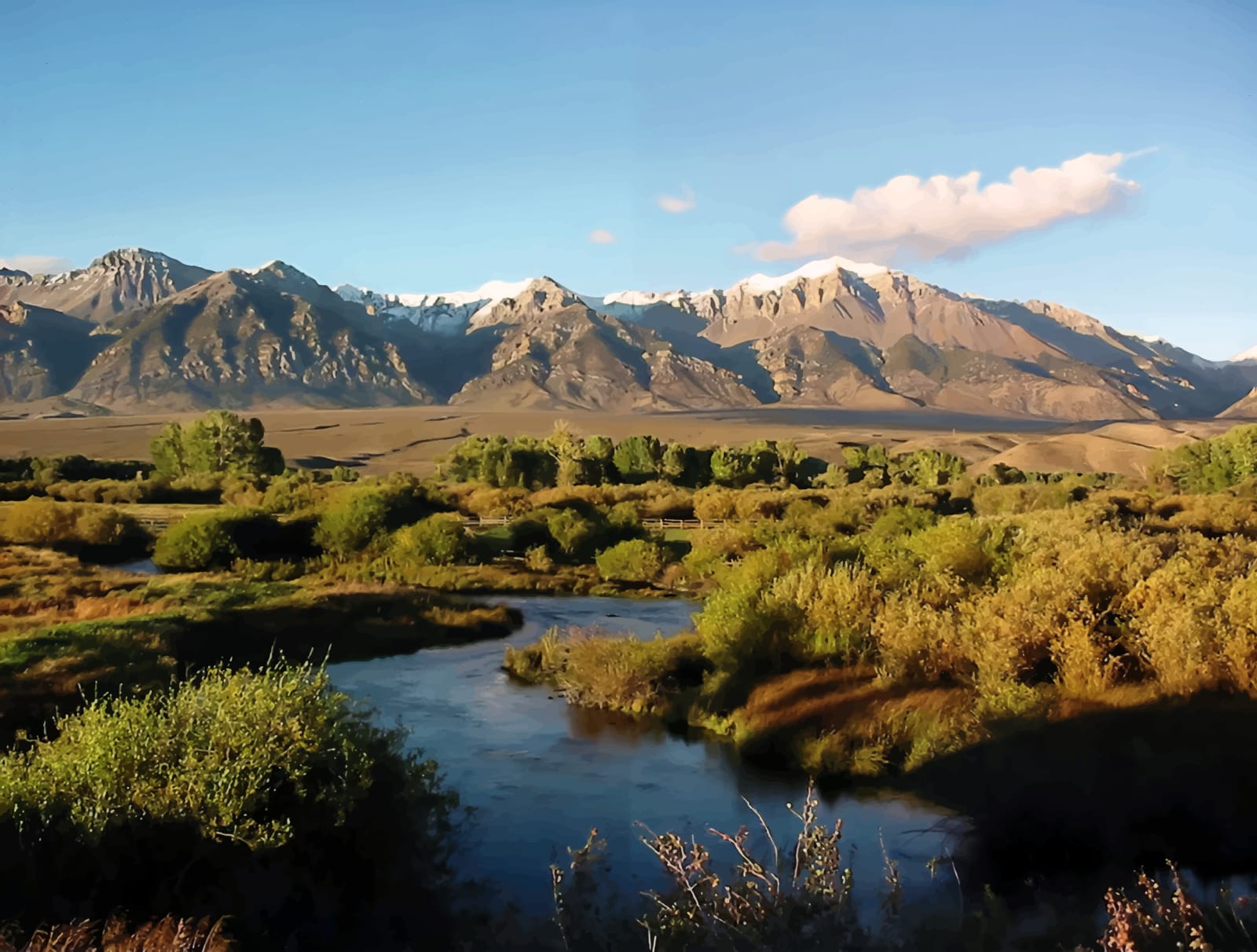 A winding river flows through a valley with lush vegetation, leading to snow-capped mountains under a blue sky.
