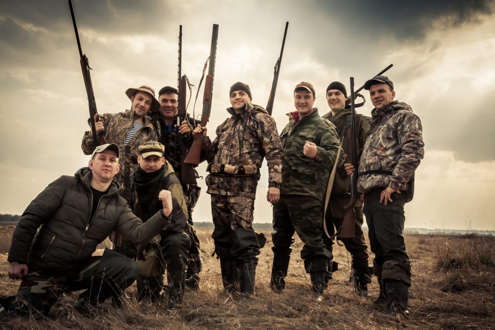 Hunters standing together against sunrise sky in rural field during hunting season. Concept for teamwork.