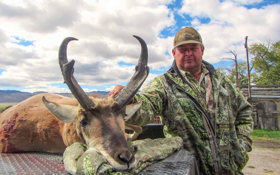 A hunter in camouflage poses with a harvested pronghorn.