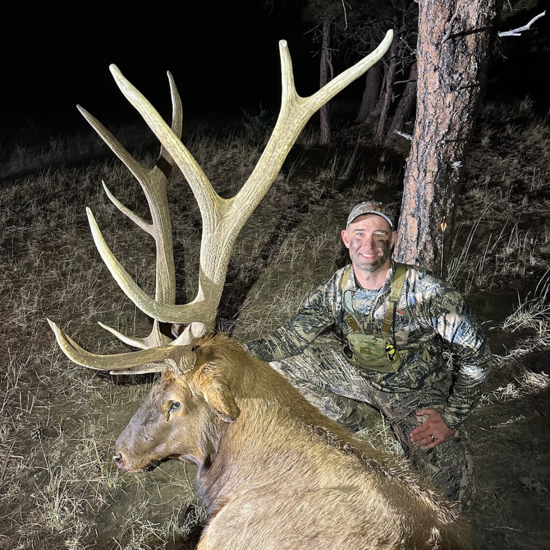 A hunter poses with a harvested elk at night.