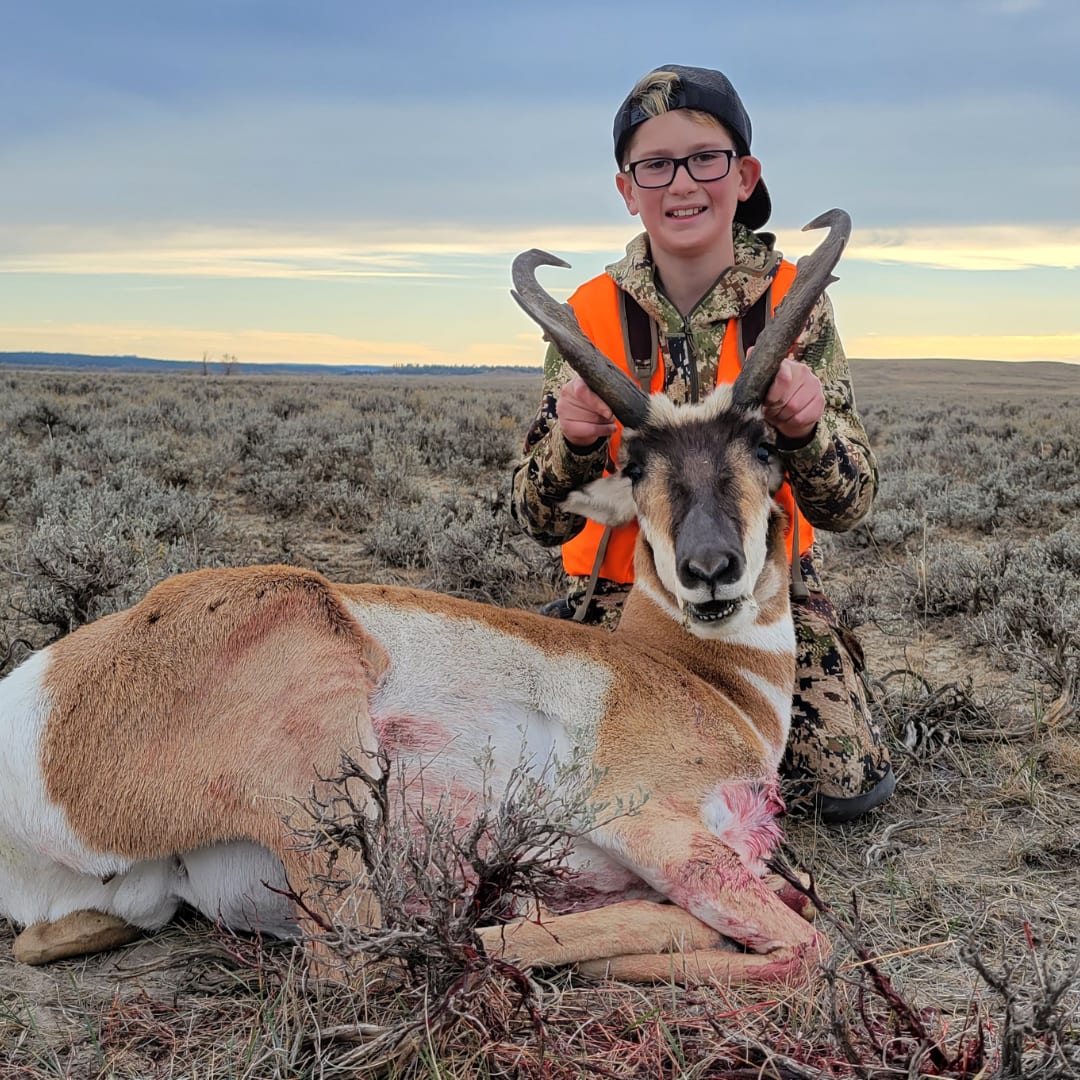 A young hunter poses with a harvested pronghorn in a field.