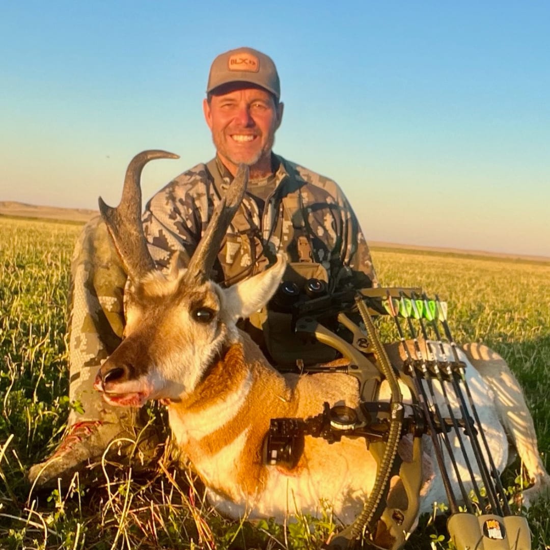 A hunter poses with a harvested pronghorn in a grassy field.