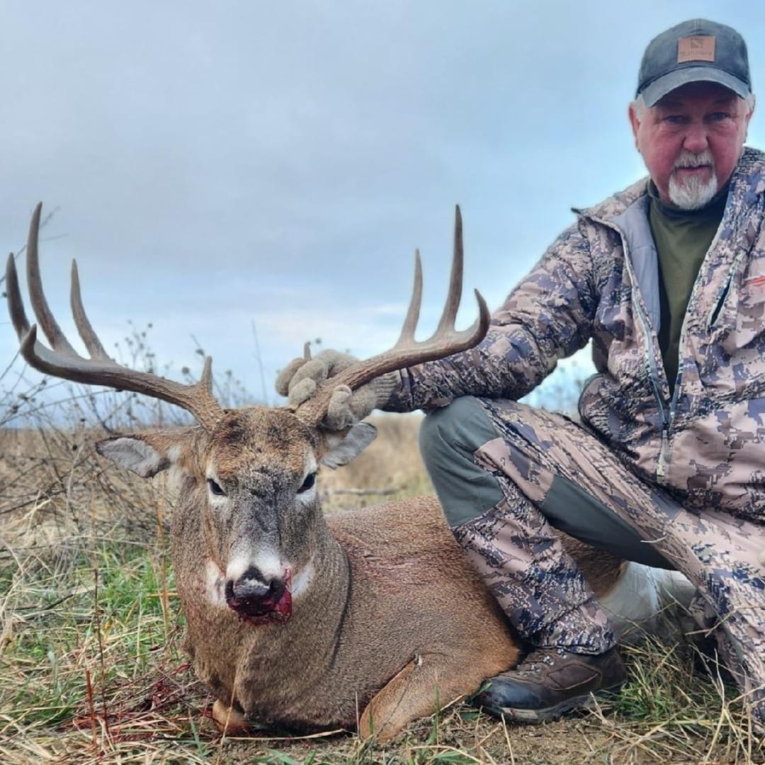 A hunter poses with a harvested whitetail deer in a field.