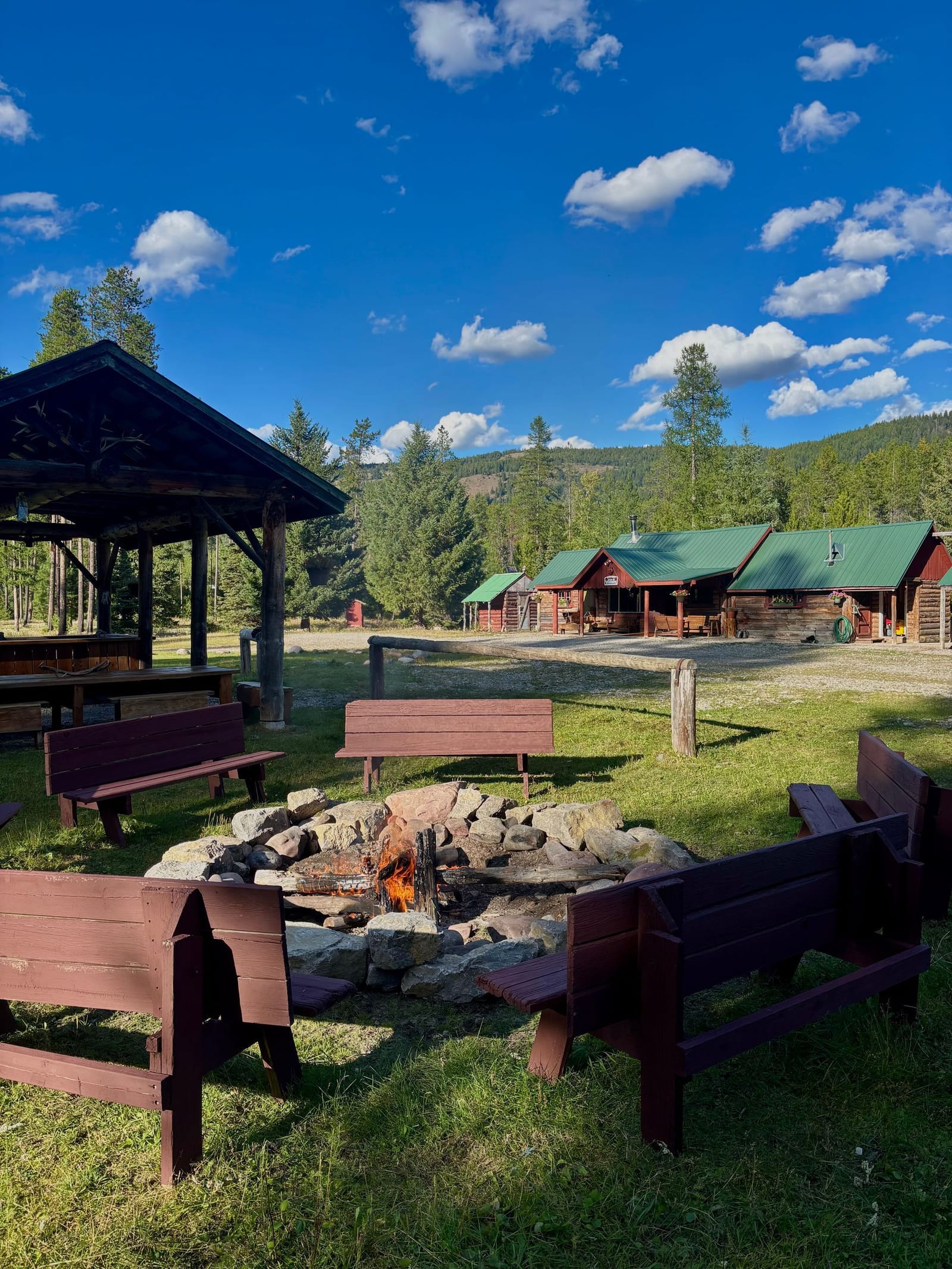 A fire pit surrounded by benches in front of cabins at a lodge.