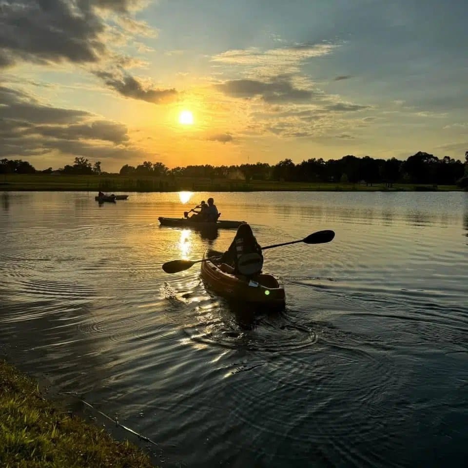 People are kayaking on a lake at sunset.