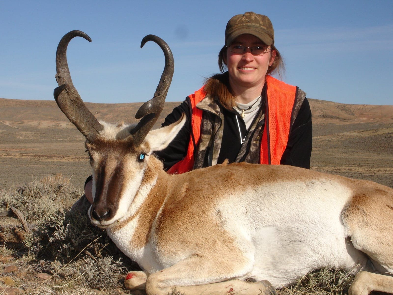 A hunter poses with a harvested pronghorn in a field.