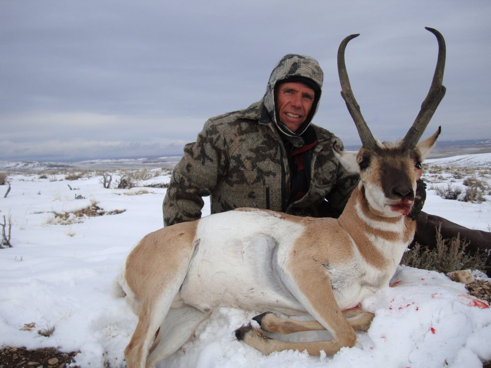 A hunter poses with a harvested pronghorn in a snowy landscape.