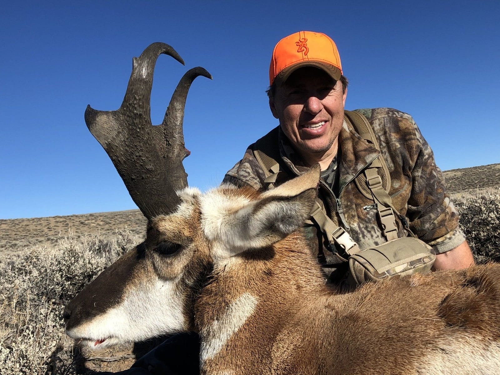A hunter poses with a harvested pronghorn under a clear blue sky.