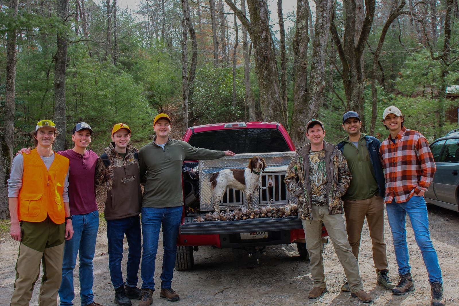 A group of hunters poses with a dog and harvested northern bobwhite quail in the back of a red truck.
