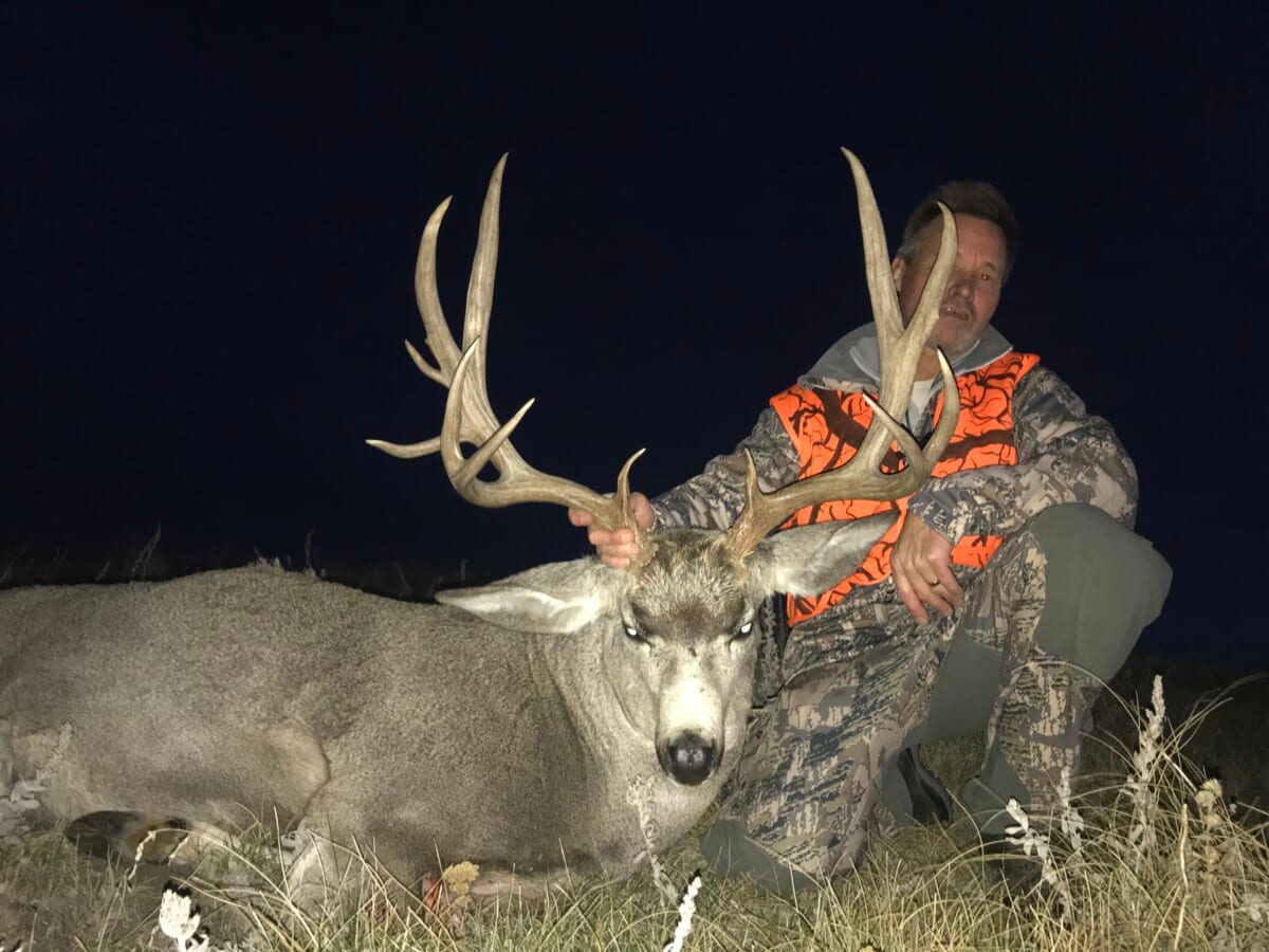 A hunter poses with a harvested mule deer at night.