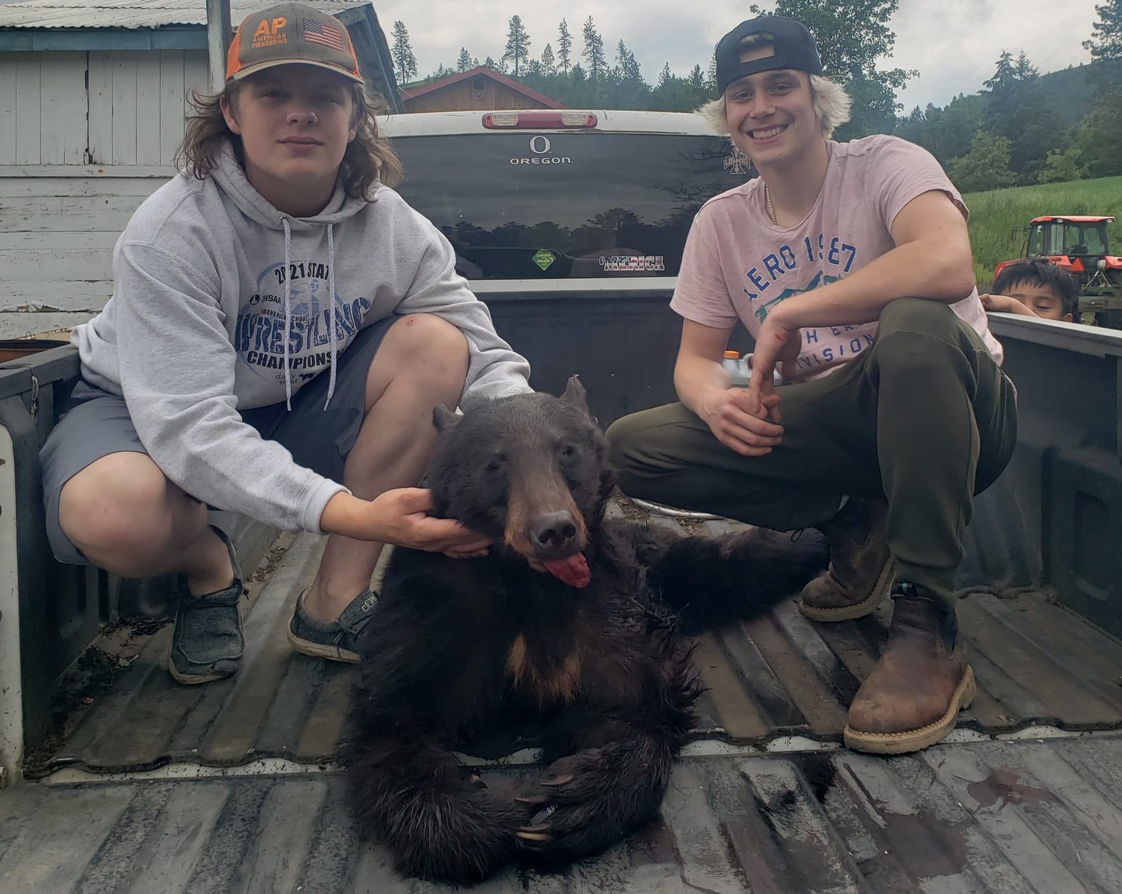 Two young men pose with a harvested black bear in the back of a pickup truck.