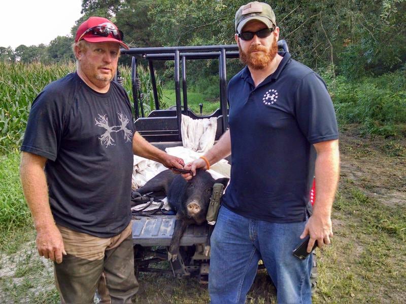 Two men pose with a harvested wild boar in the back of a utility vehicle.