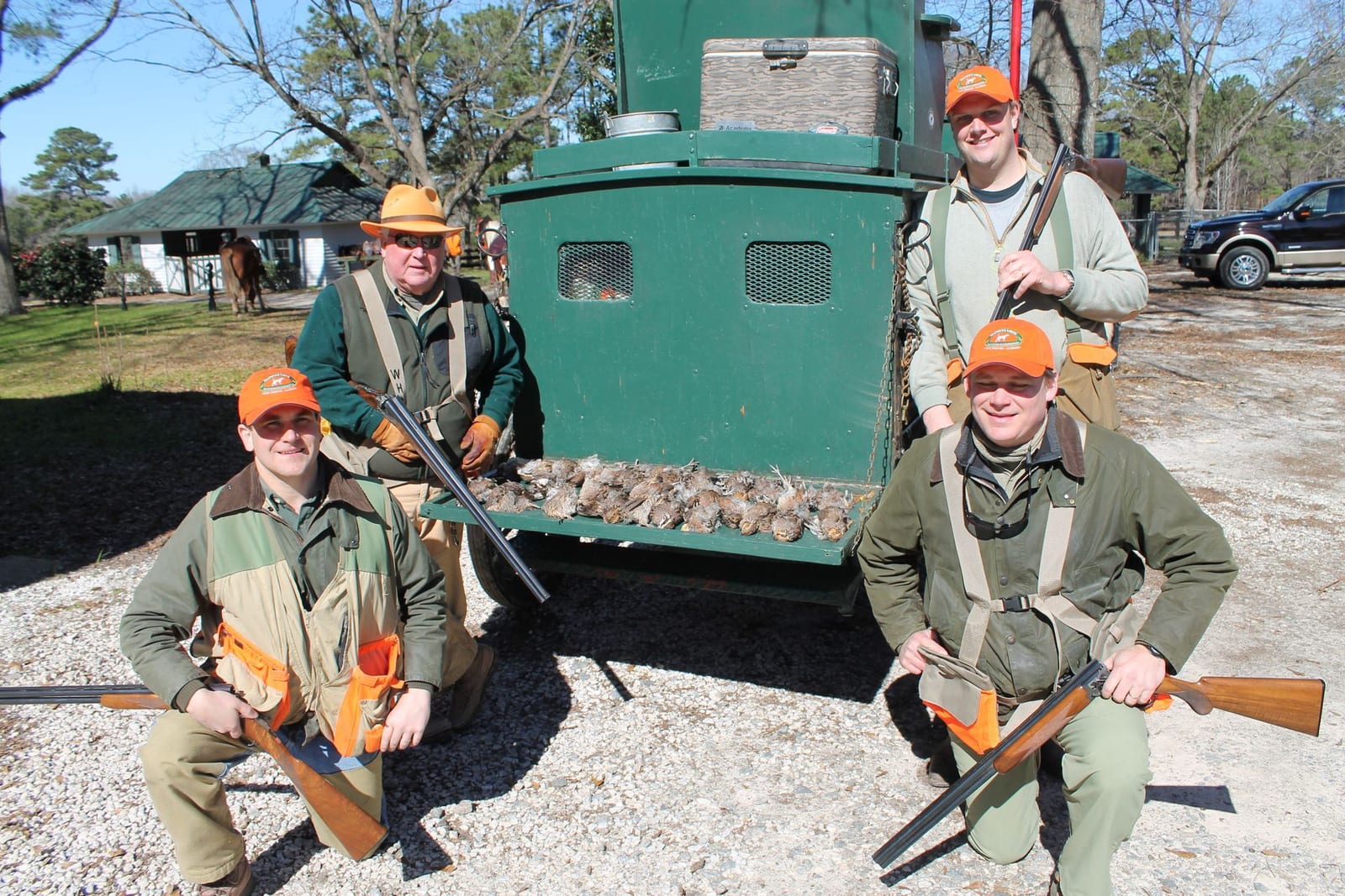 Four hunters pose with their shotguns and a pile of harvested northern bobwhite quail next to a green hunting vehicle.